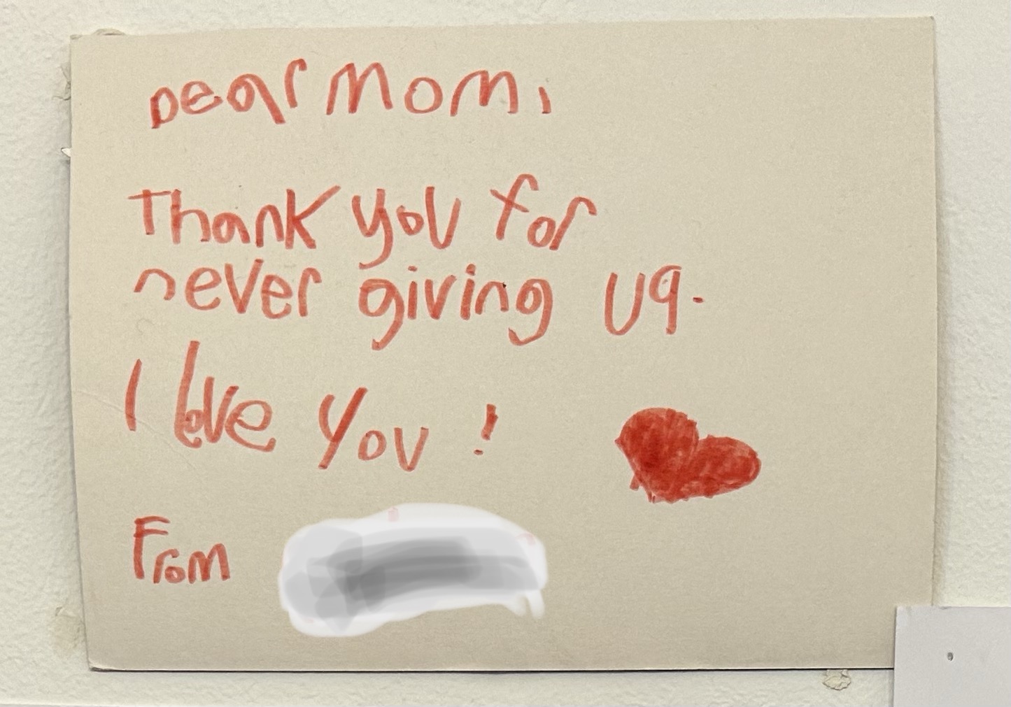 note from child in red ink on white paper reading: dear mom, thank you for never giving up, I love you. the p in up is written reversed, a typical mistake of children learning to write.