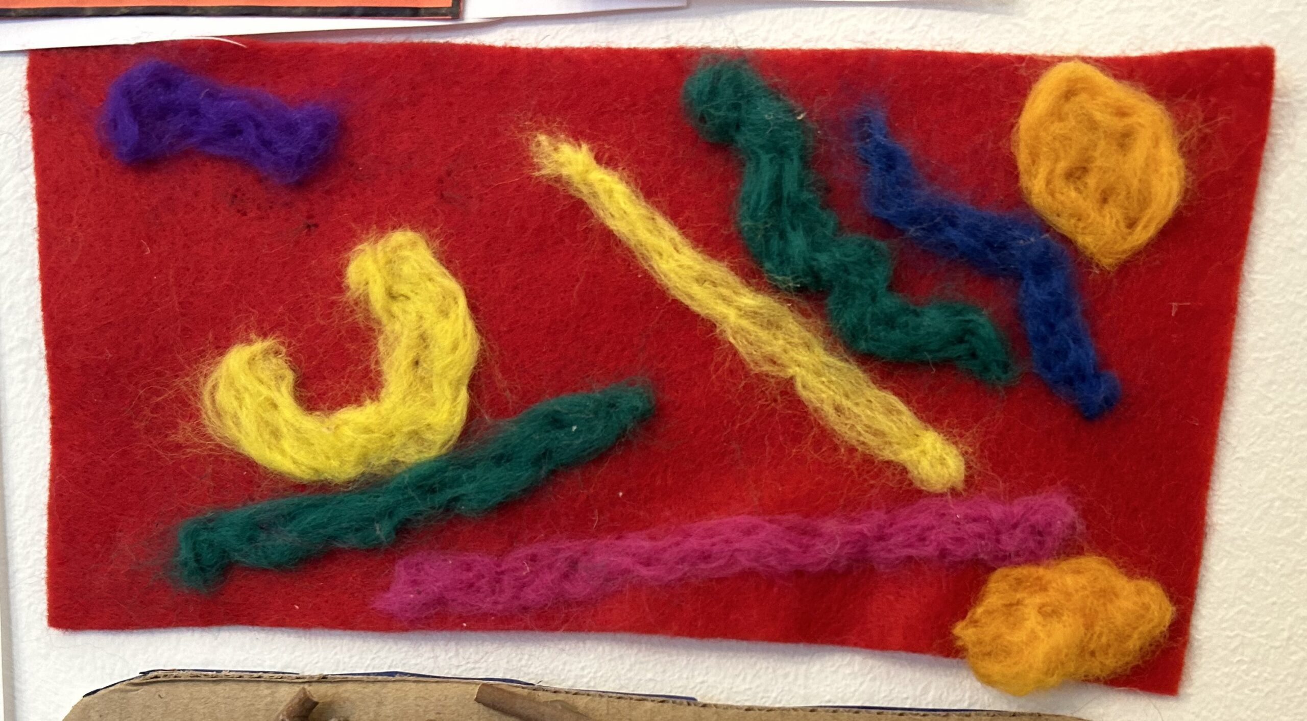 multiple felt scraps of green, yellow, blue and pink or a red felt background, made by a child
