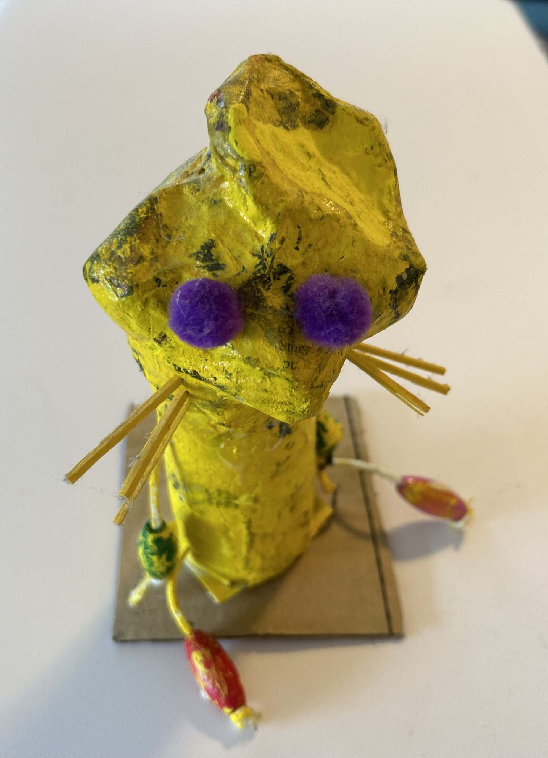 a yellow paper mache creature with purple puff eyes and toothpick extremities made by a child