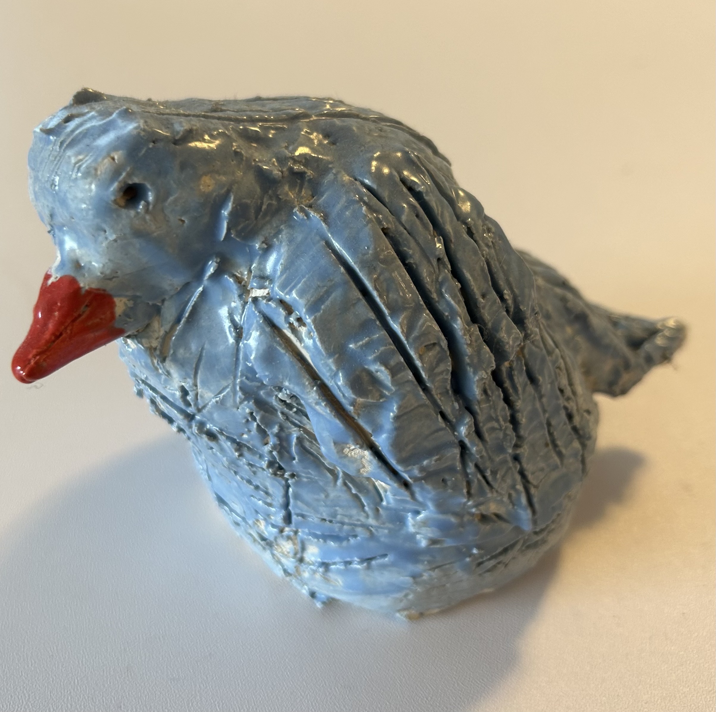 a painted sculpture of a blue colored bird sitting with an orange beak, by a child