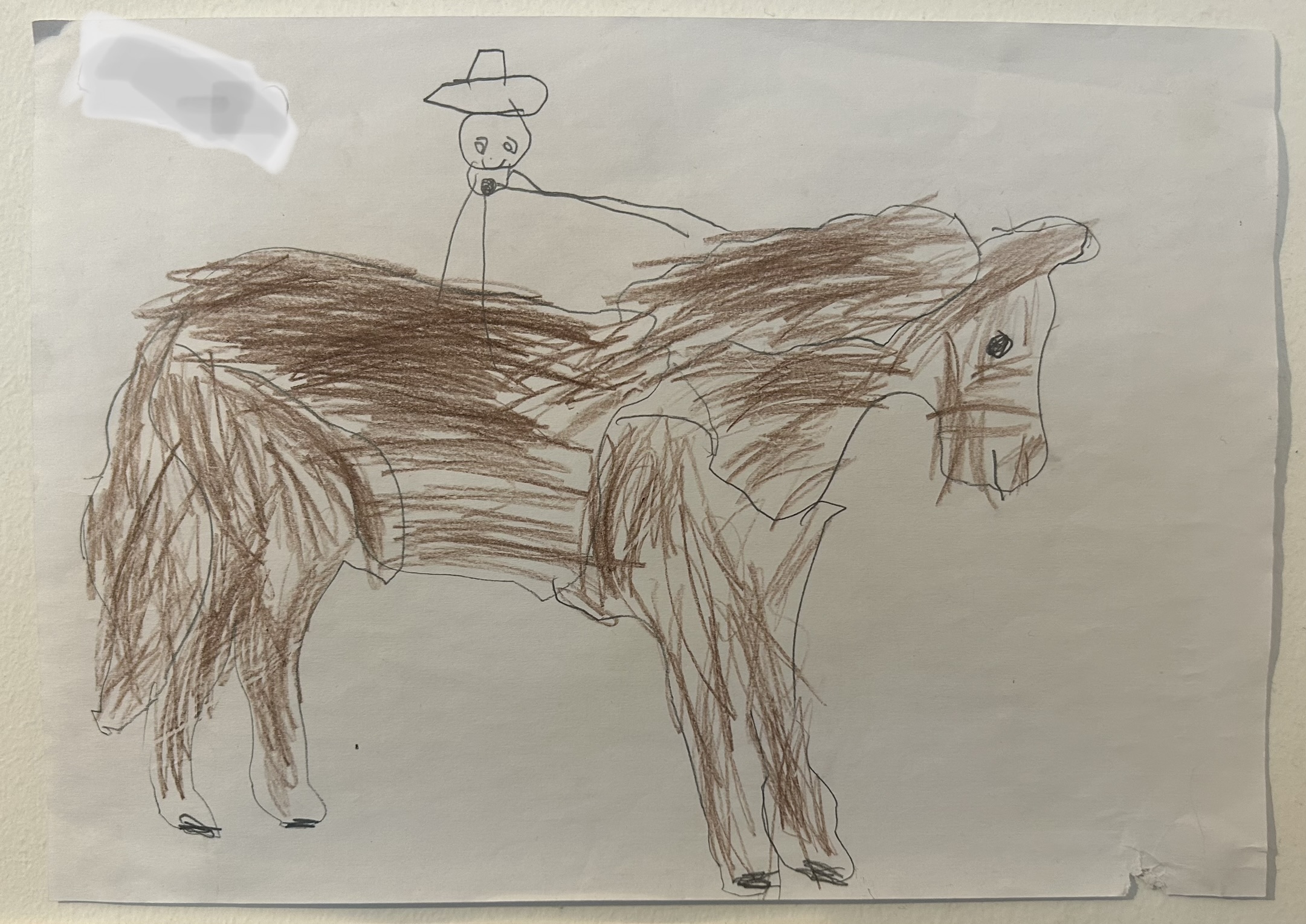a brown crayon drawn horse on white paper with a stick figure riding on top with a cowboy hat, drawn by a child