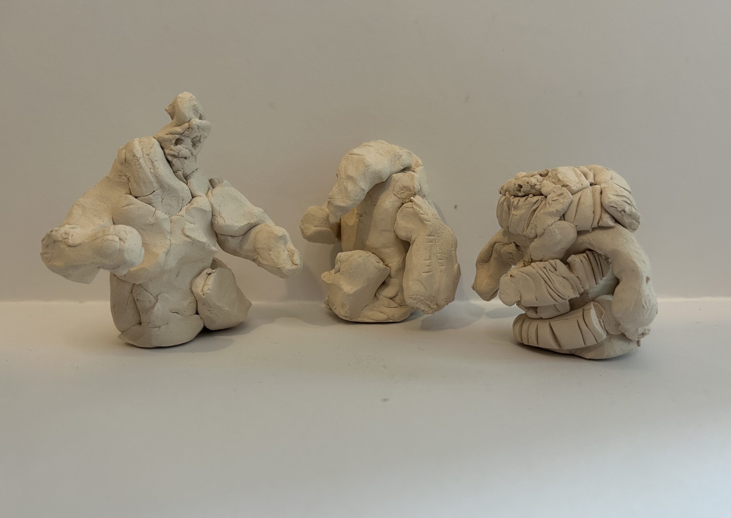 3 abstract creature-humanoid clay sculptures places as though they are having a conversation in a semi-circle, all by a child